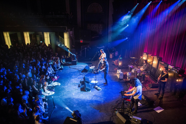 Band on stage under blue lighting with fans lined along the stage