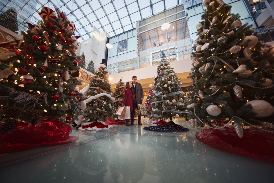 Couple shopping at a mall looking at the Christmas tree display and decor.
