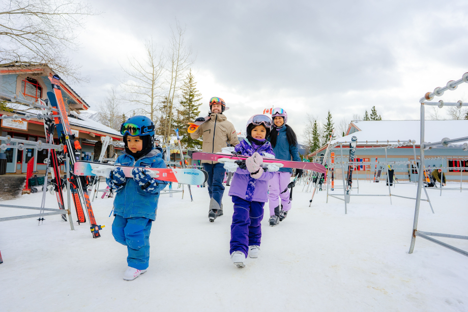 A family walks through the ski rack area at Nakiska, carrying their skis before a day on the slopes.