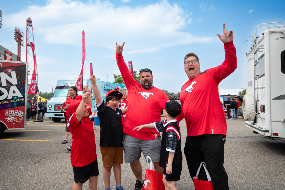 Fans wearing Stampeders shirts holding their arms up cheering with food trucks in the background